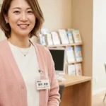 障害のある子どもの成人移行期の入浴介助と介護制度についてクリニック相談室で優しく微笑むピンクカーディガン姿 of 女性アドバイザーの横長写真