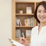 術後や入院後の清潔ケアと在宅入浴の再開について解説する白ブラウスを着てクリップボードを持つ女性アドバイザーの横長写真