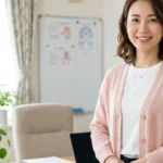 レット症候群のある子どもの入浴ガイドと手の常同運動・呼吸不整対応についてクリニック相談室で優しく微笑むピンクカーディガン姿 of 女性アドバイザーの横長写真